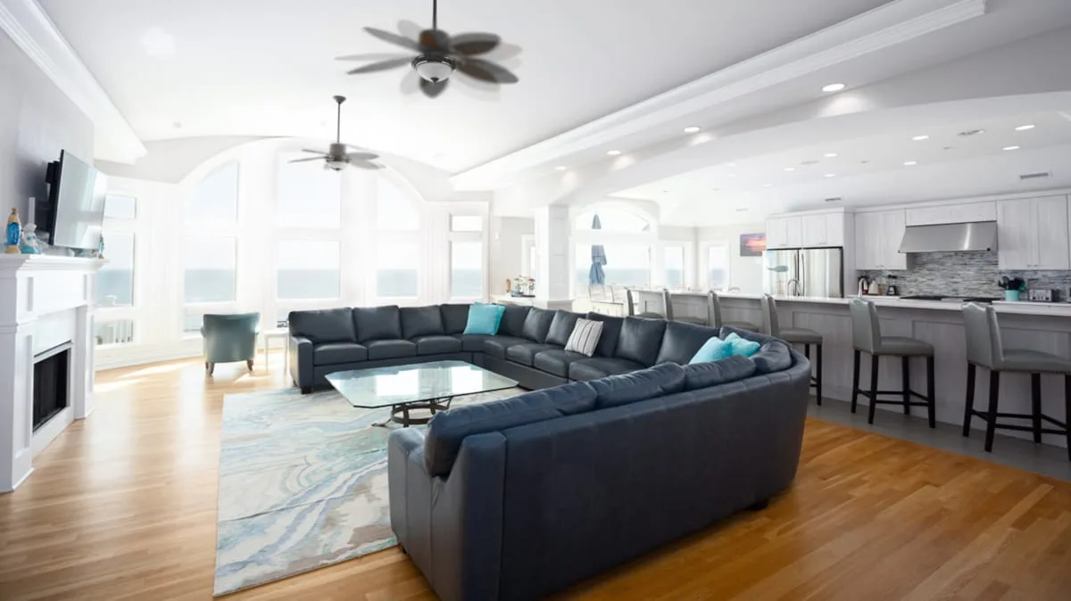 A bright open-plan living room with dark seating and a kitchen island.