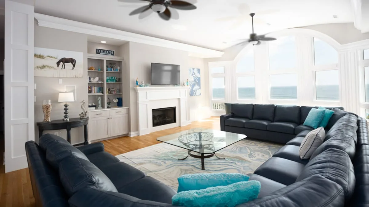 A bright living room with dark seating arranged around a glass coffee table.