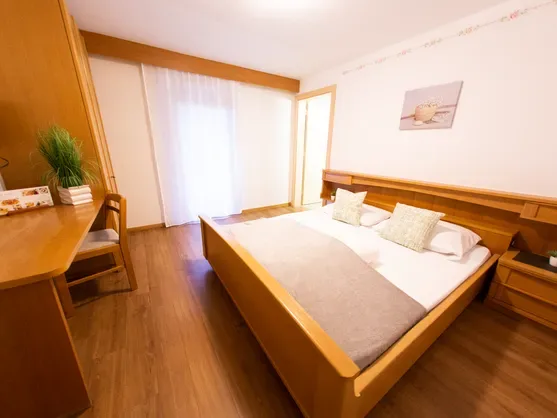 Acogedora habitación doble con cama de madera clara, escritorio, televisor y suelo laminado