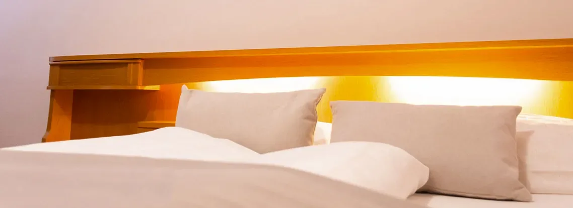 Acogedora cama doble con almohadas blancas e iluminación indirecta, en una habitación de ambiente cálido