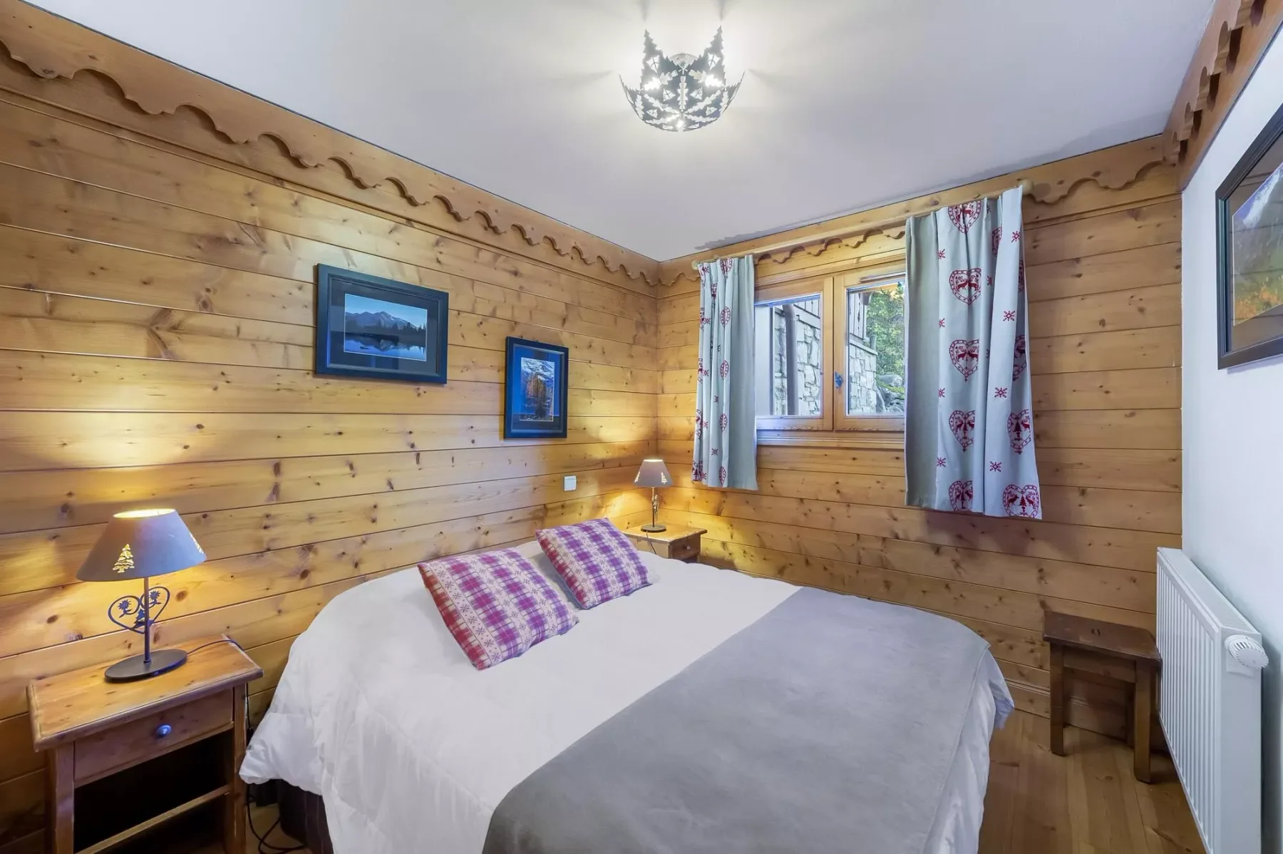Un dormitorio revestido de madera con una cama bajo una ventana con cortinas estampadas.