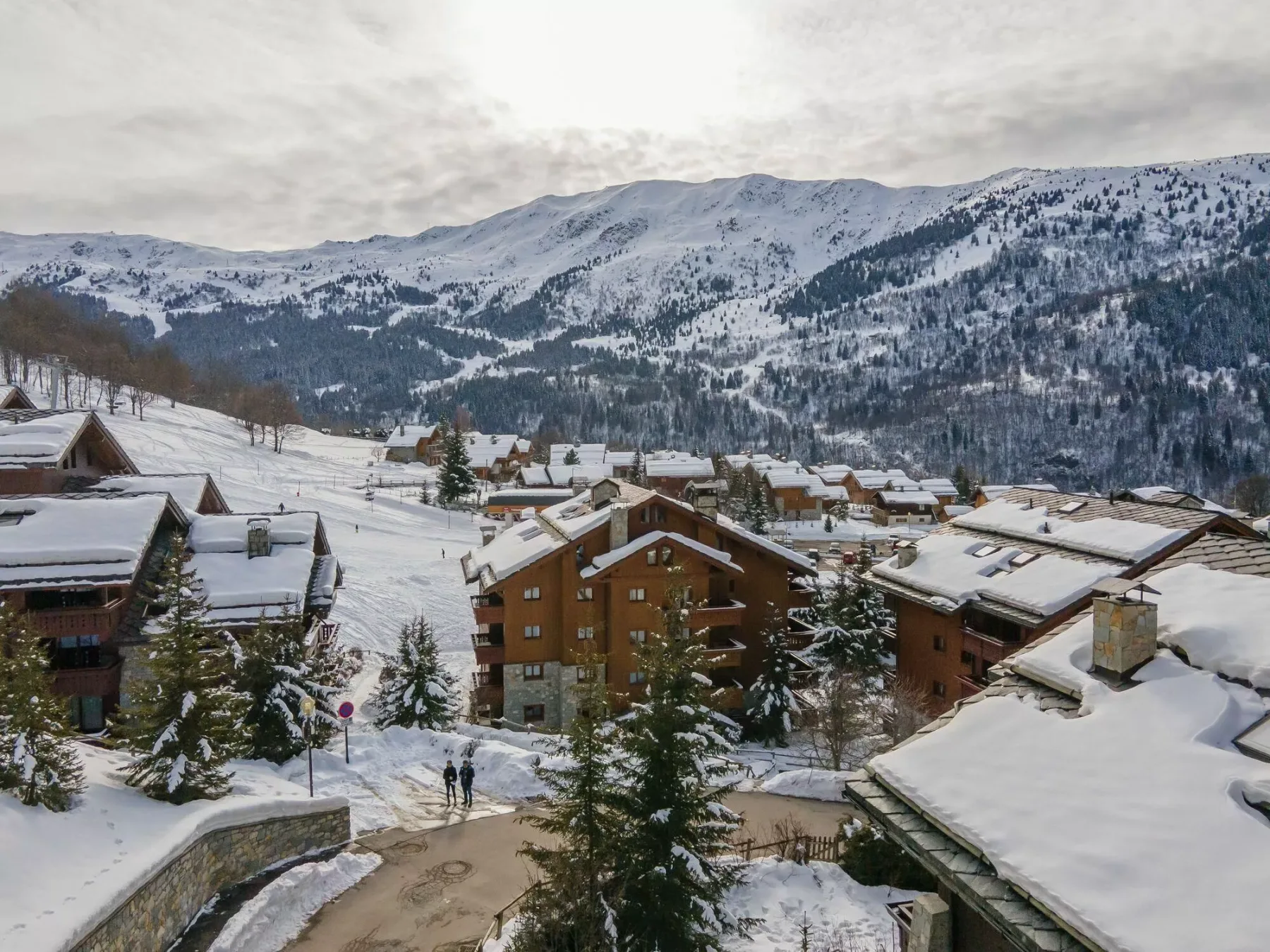 Un pueblo de montaña nevado con edificios agrupados y laderas boscosas.