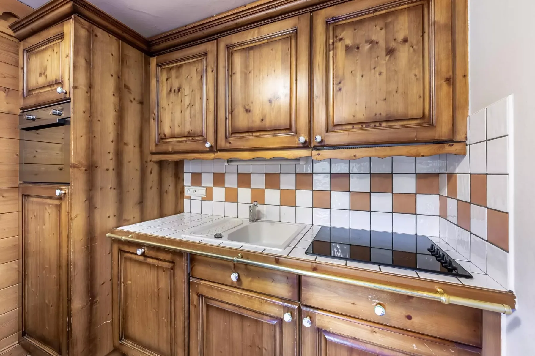 Una cocina con gabinetes de madera, salpicadero de azulejos, fregadero y estufa.
