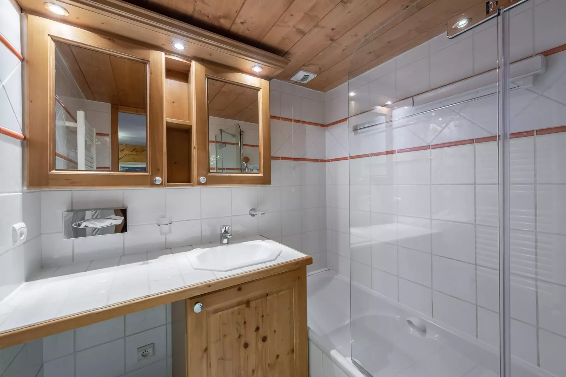 Un baño alicatado con mueble de madera, armarios con espejo y ducha.