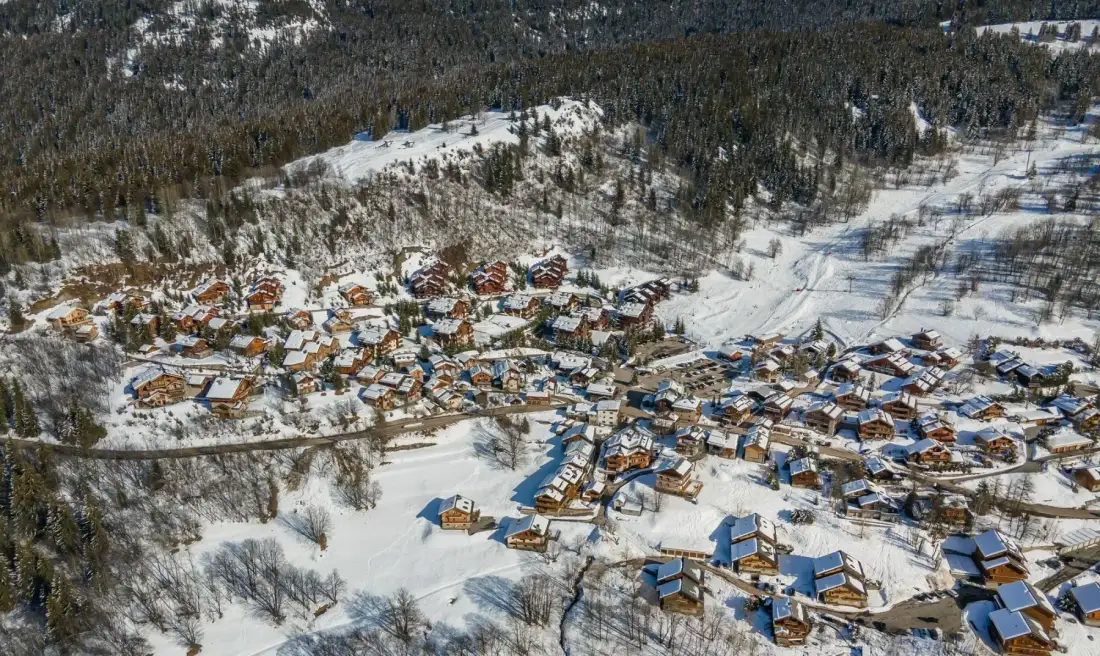 Vista aérea de un pueblo de montaña nevado rodeado de bosque.