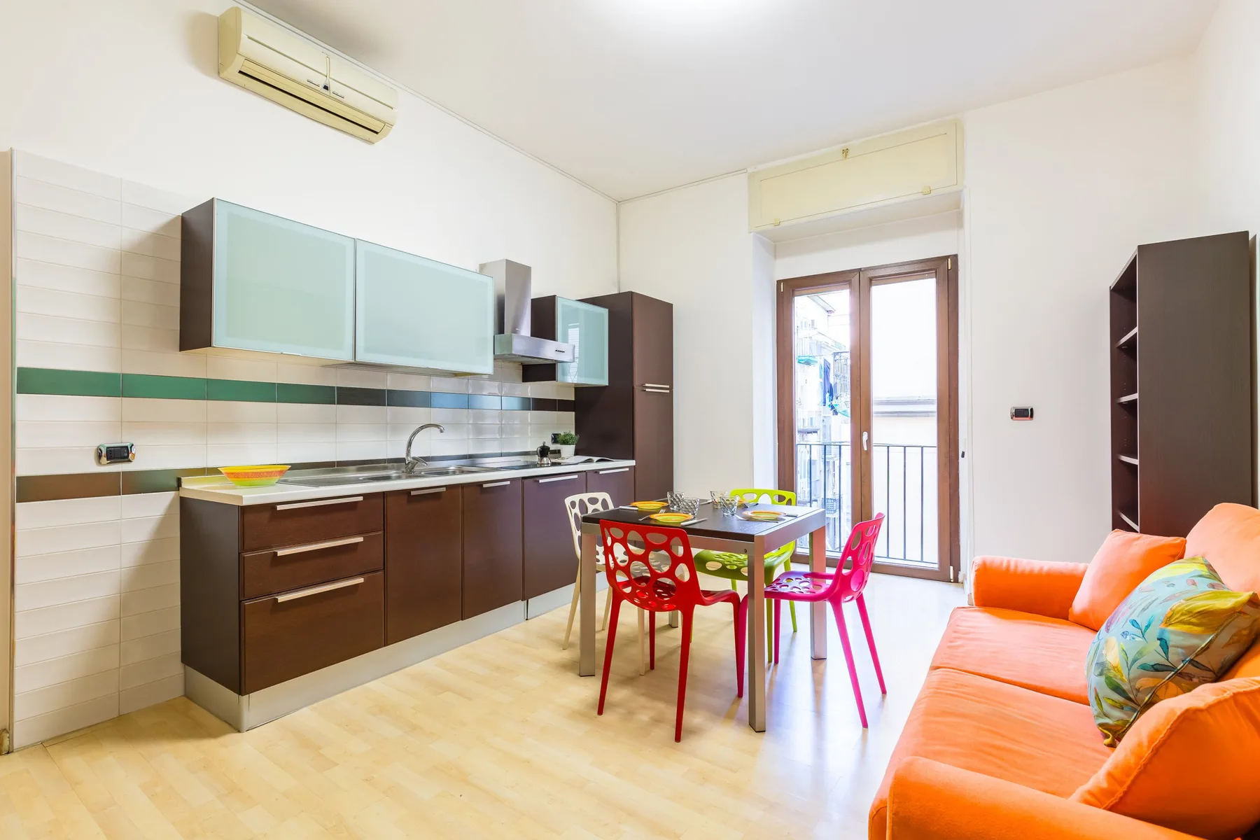 A bright kitchen and dining area with a table beside an orange sofa.