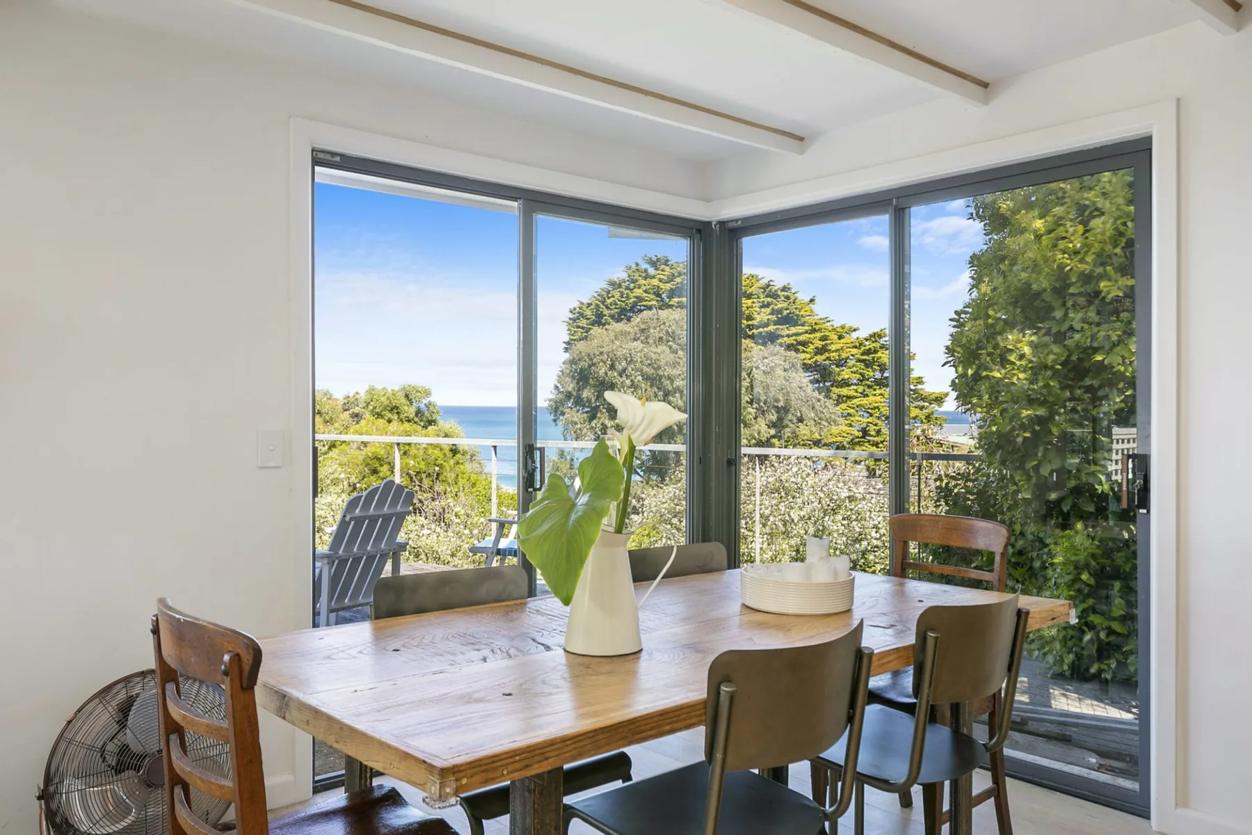 Comedor con una mesa de madera junto a grandes ventanales con vistas a la vegetación y al océano.