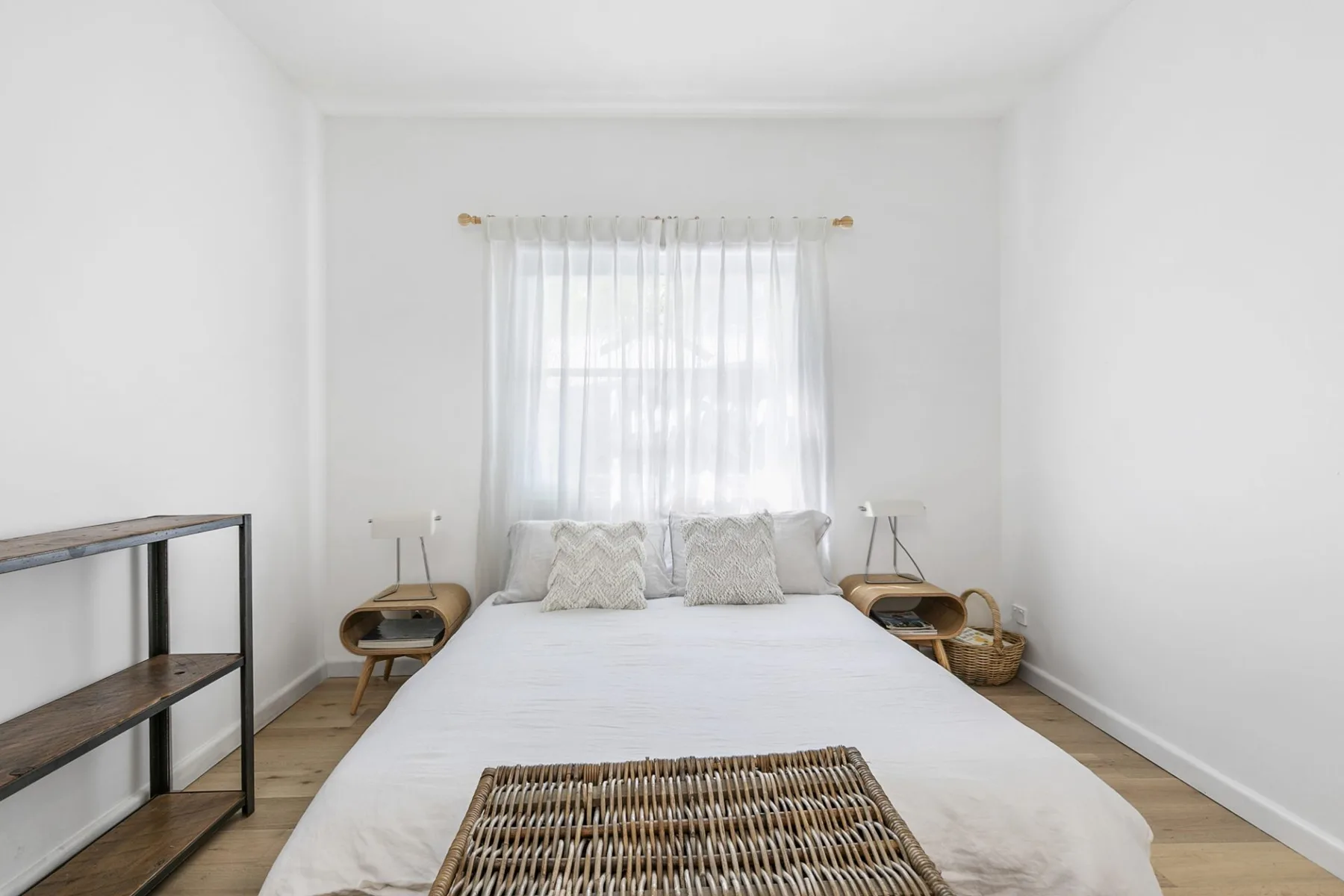 Un dormitorio luminoso con una cama bajo una ventana con cortinas translúcidas.