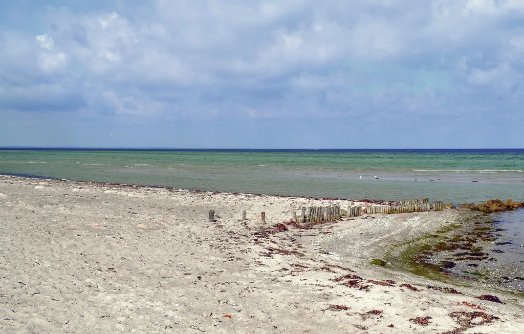 A sandy shoreline meets shallow water beneath a cloudy sky.