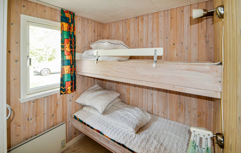 A compact bunk-bed room with wooden wall paneling and a window.