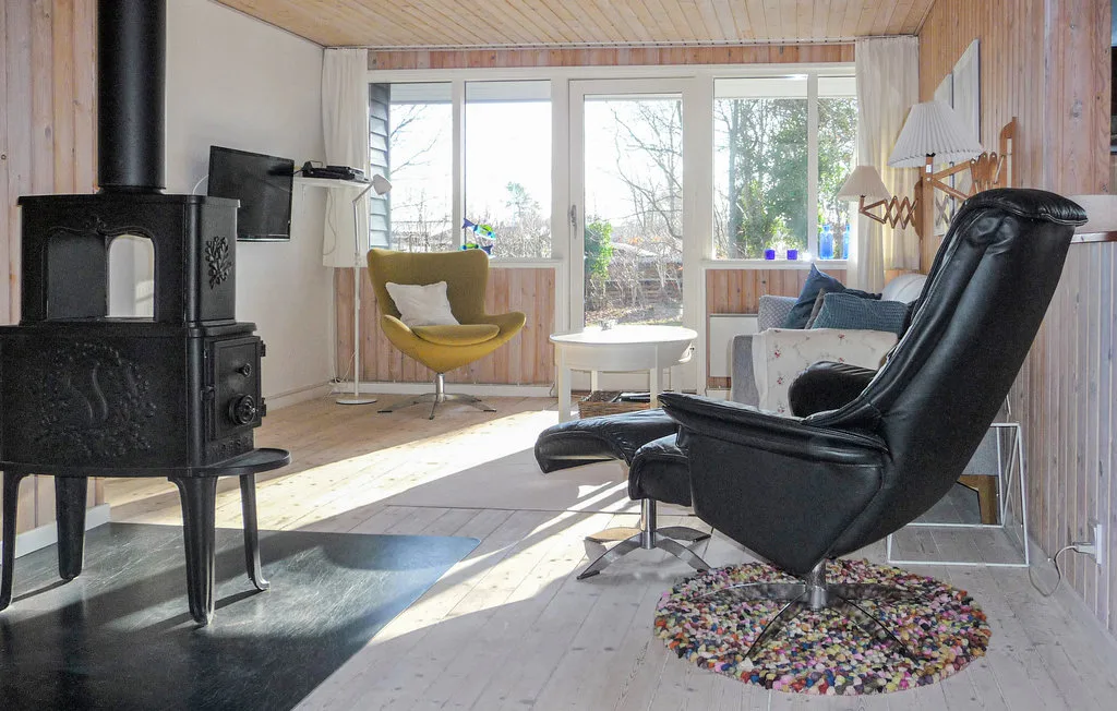 A bright living room with a wood-burning stove and seating beside large windows.