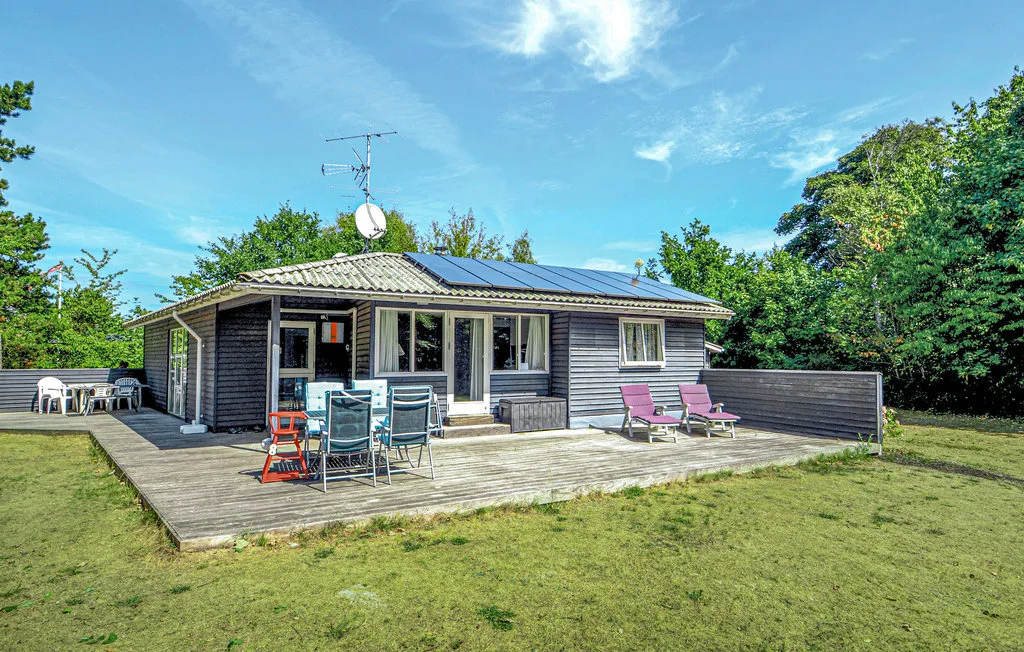 A low house opens onto a broad wooden deck with outdoor seating and a lawn.