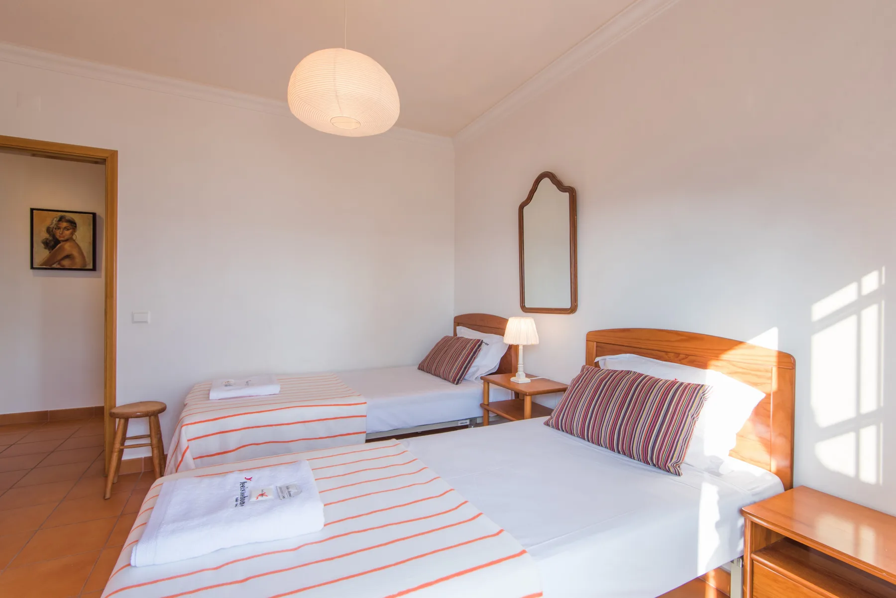 Un dormitorio luminoso con dos camas, ropa de cama a rayas y una mesita de madera.