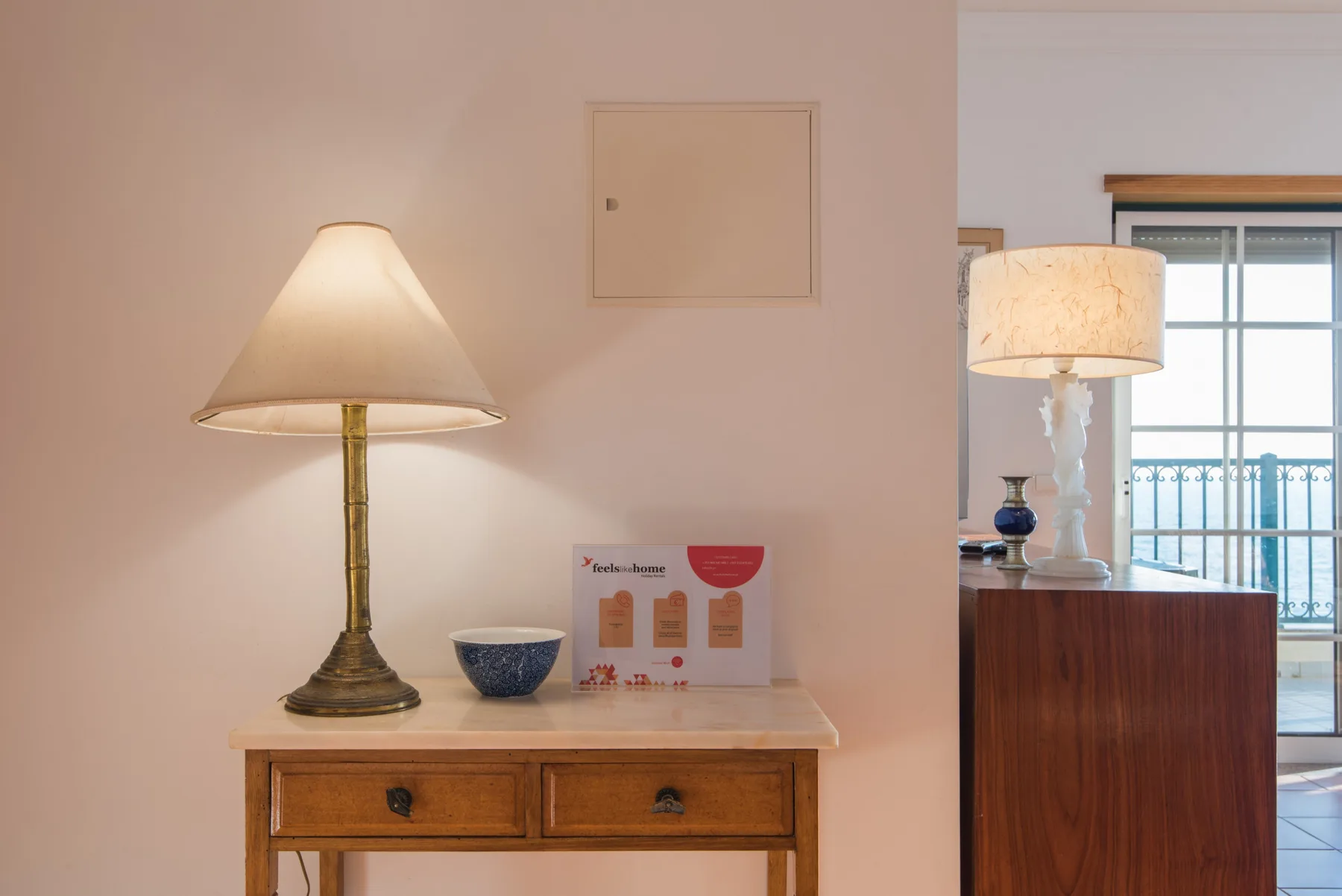Una sala de estar con una consola de madera, lámparas y una ventana con vistas a un balcón.