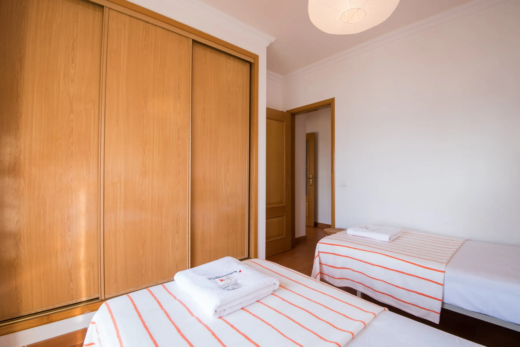 Dormitorio con dos camas, ropa de cama a rayas y un armario de madera.