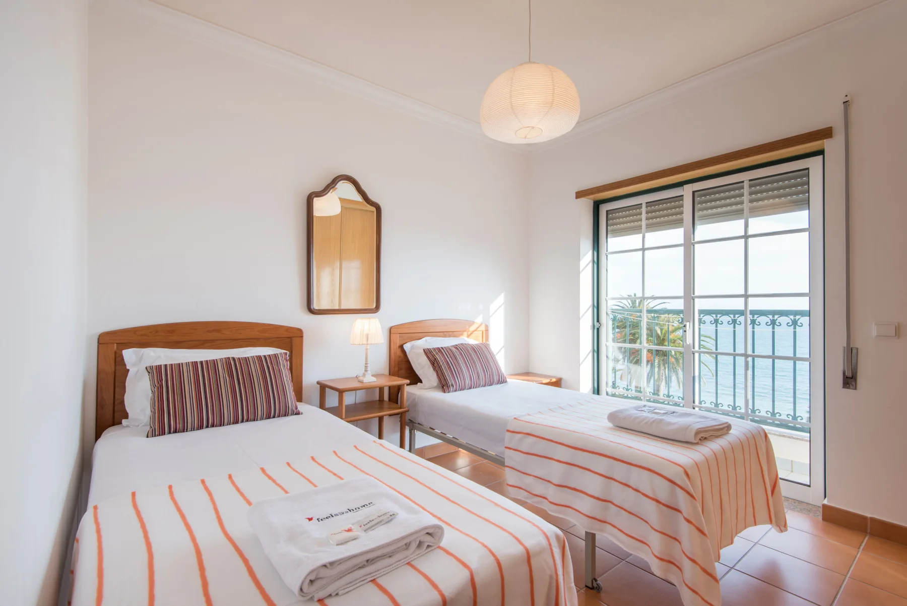 A bright bedroom with two beds and a large window overlooking a balcony.