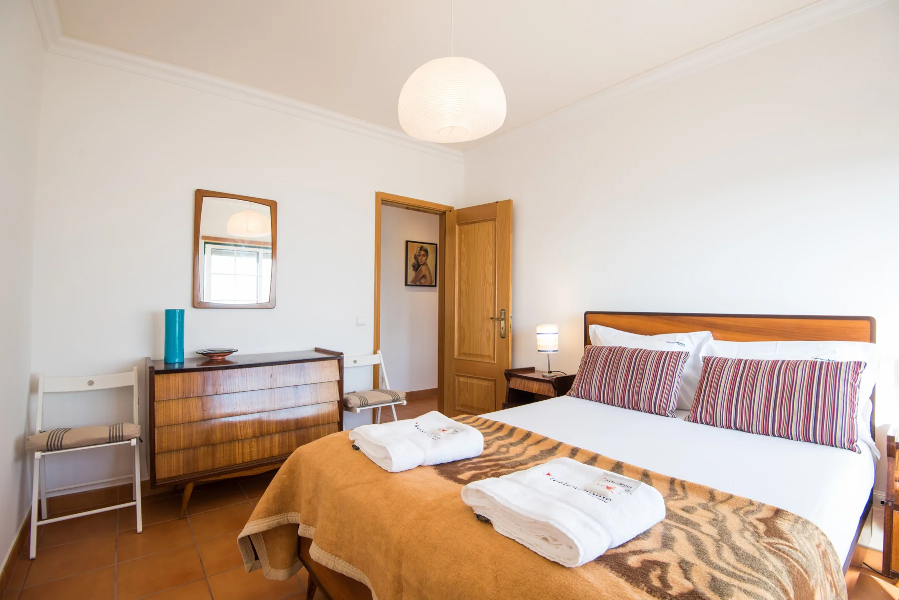 Dormitorio con cama doble, toallas dobladas y una cómoda de madera.