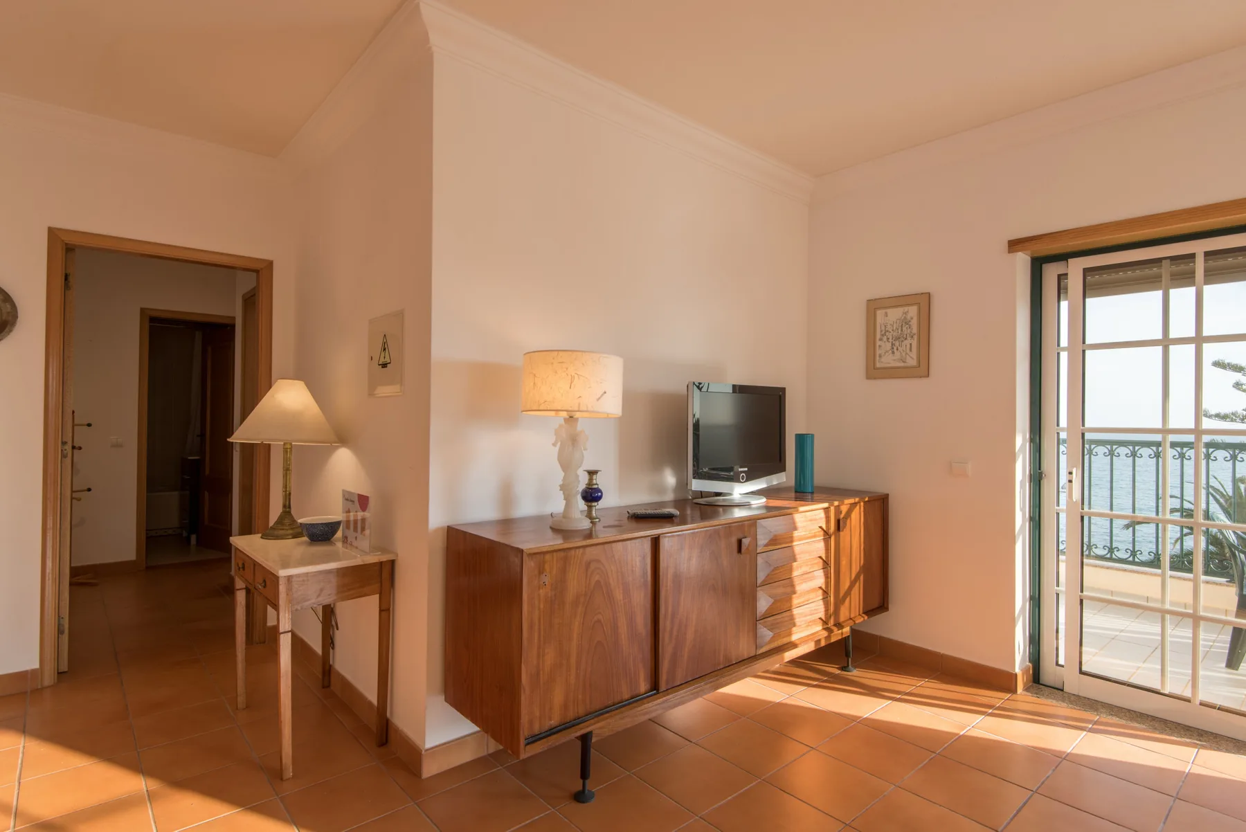 Una sala de estar con aparador de madera, televisor y puertas de vidrio que dan a un balcón.
