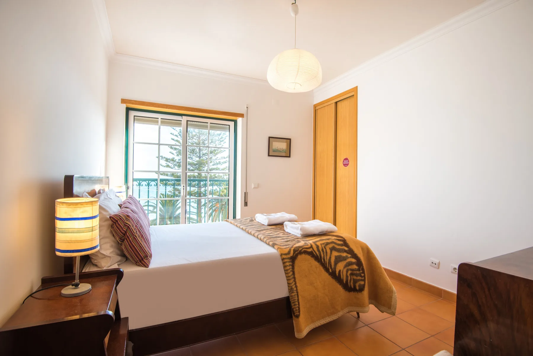A bedroom with a made bed and a large window overlooking greenery.