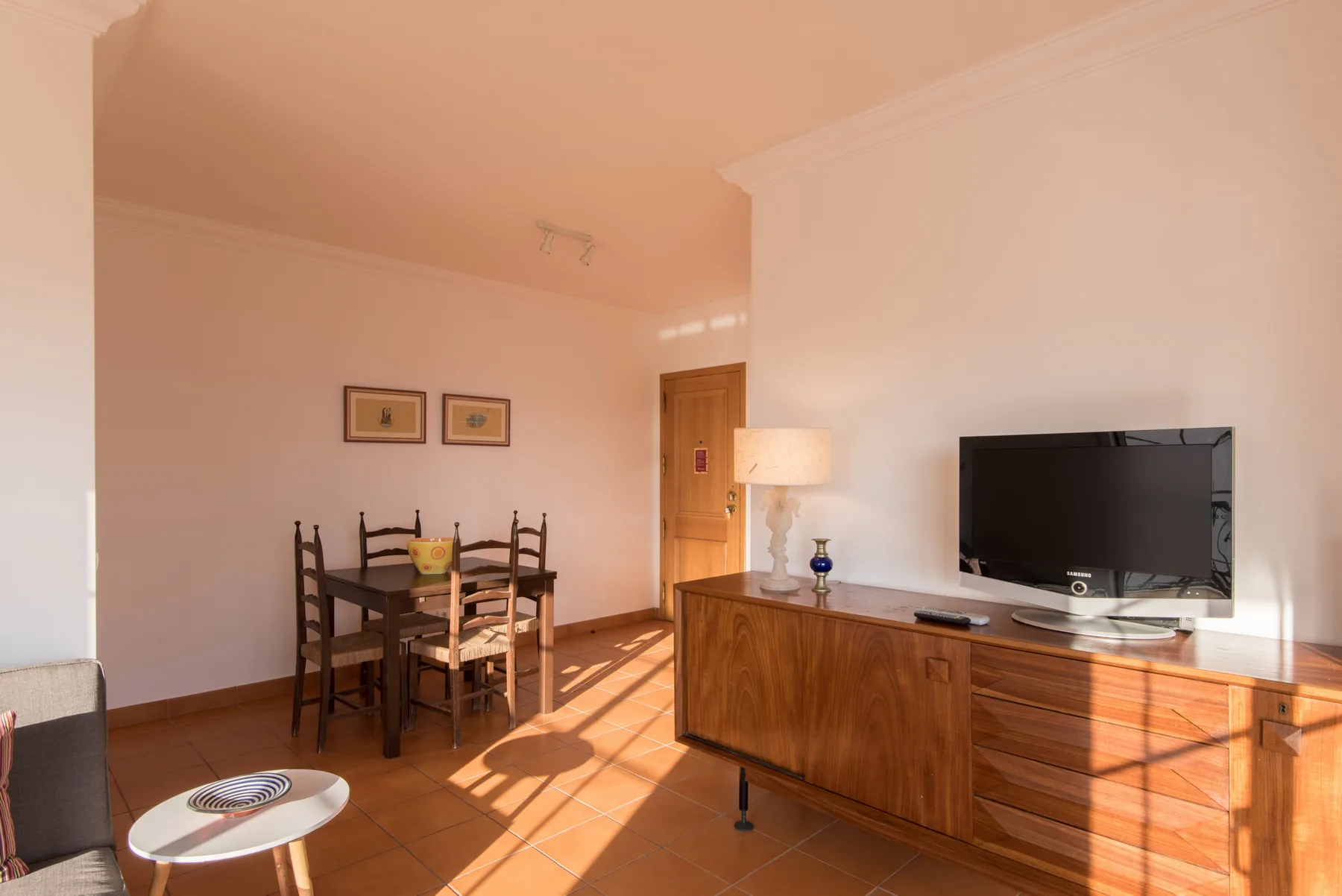 Una zona de estar y comedor con mesa de madera, asientos y televisor.