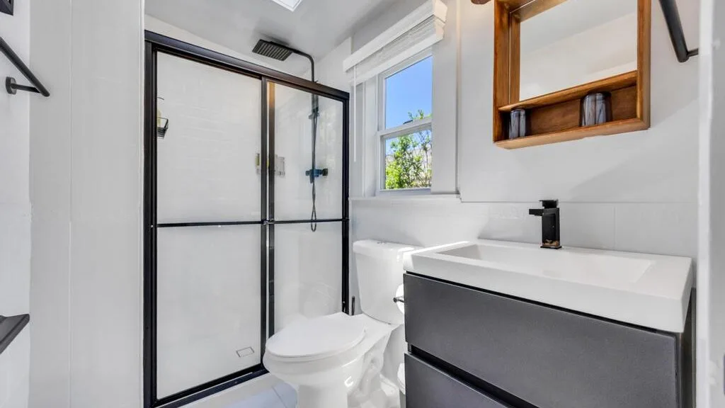 A bright bathroom with a glass shower, toilet, and vanity.