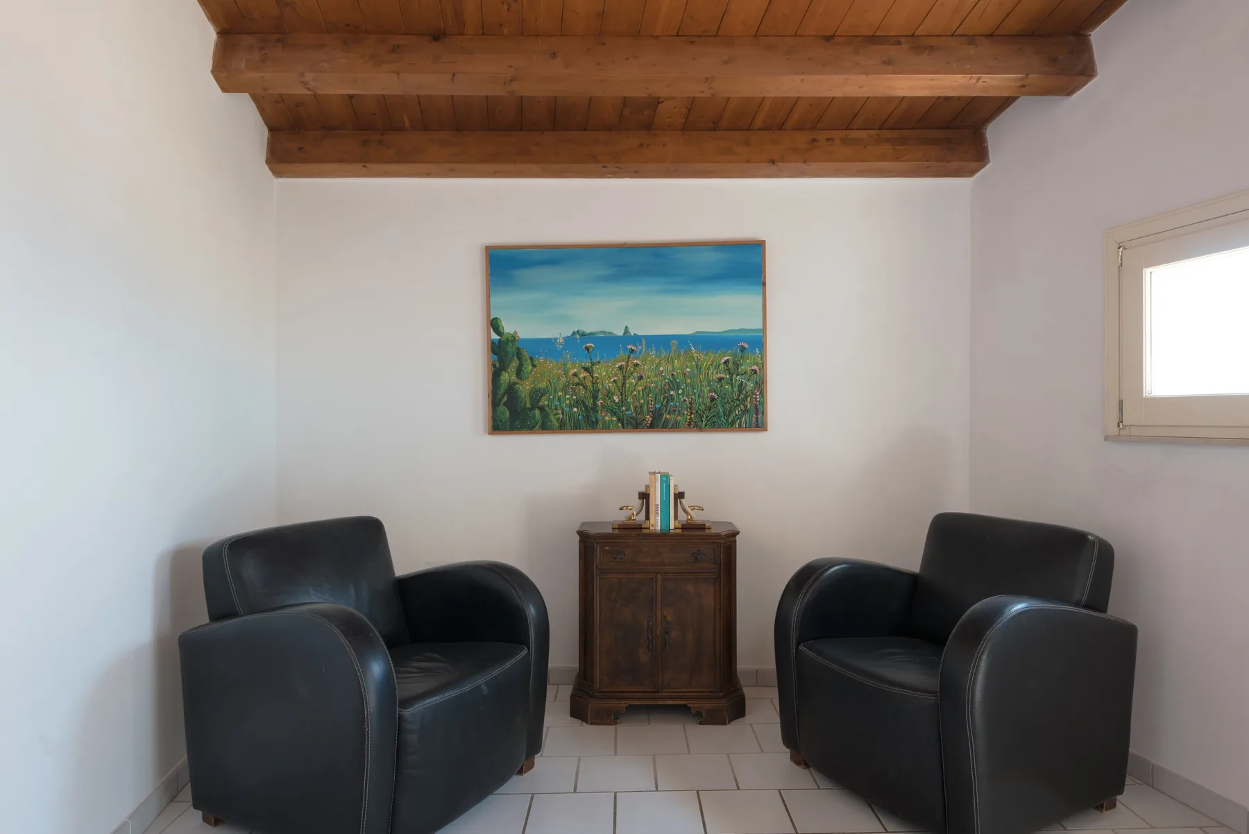 A sitting room with dark seating, a wooden cabinet, and a framed landscape painting.