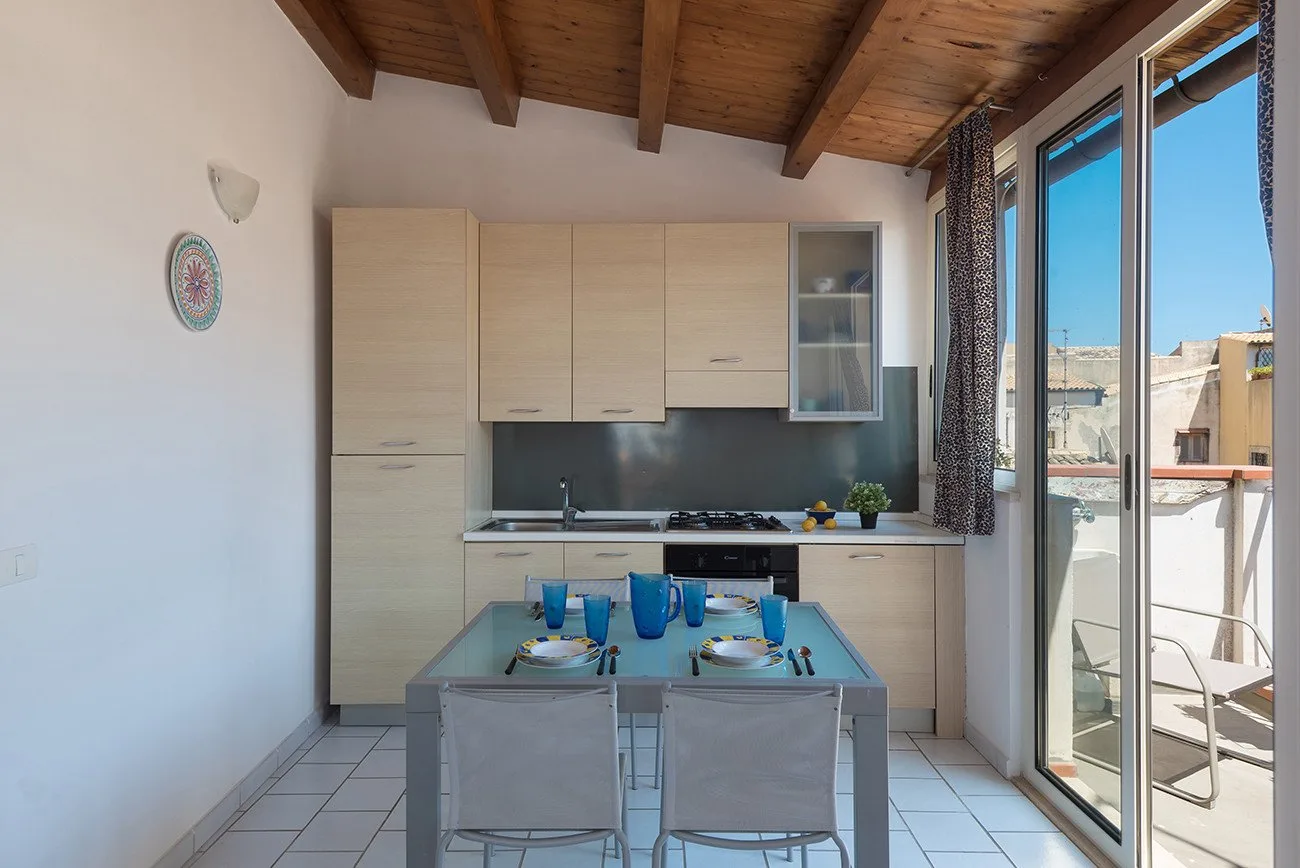 A compact kitchen and dining area with light wood cabinets and a glass table.