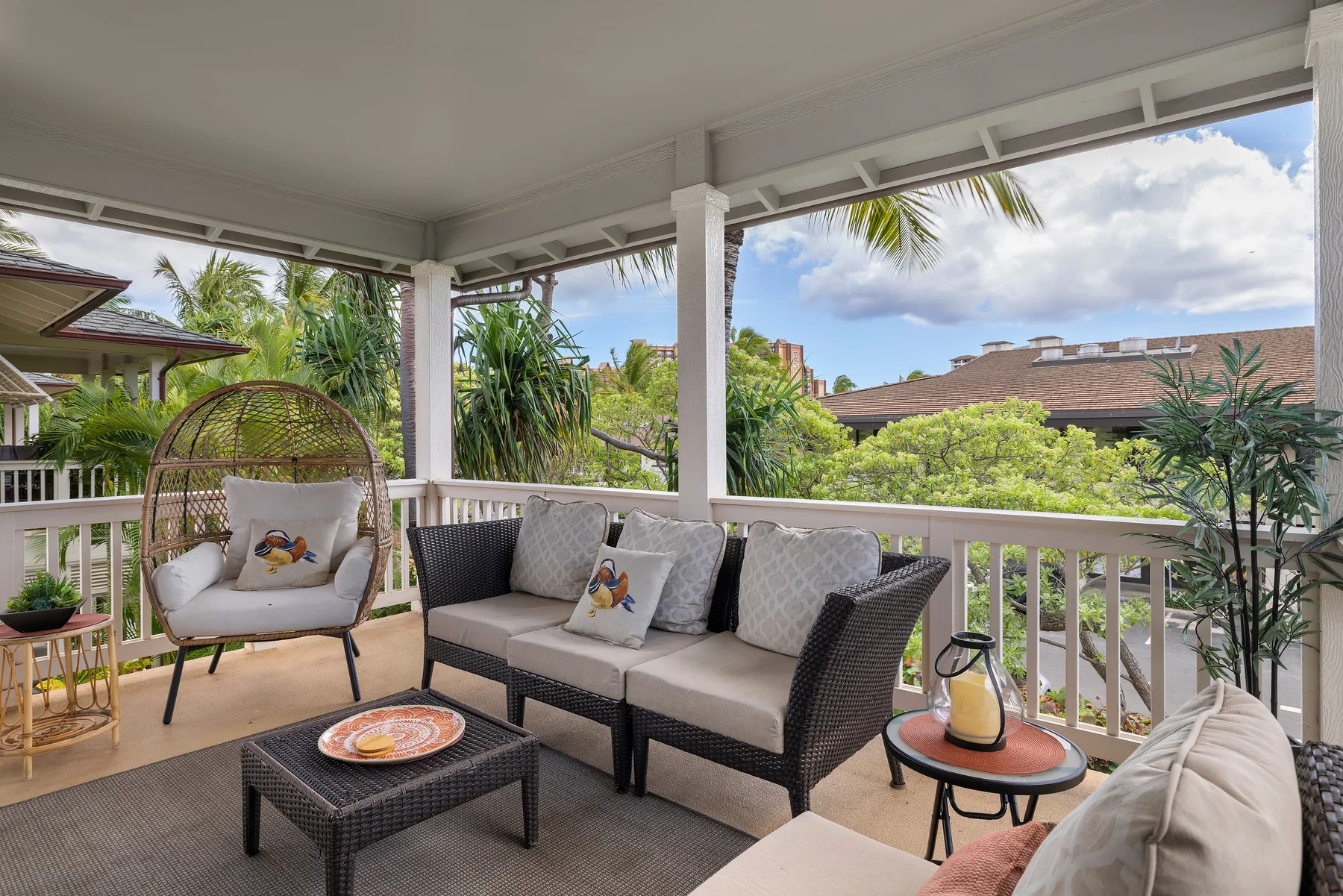 Una zona de estar exterior cubierta con muebles de mimbre acolchados y vegetación tropical.