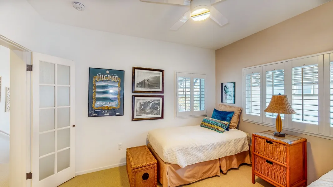 Un dormitorio con una cama, cuadros en la pared y ventanas con persianas.