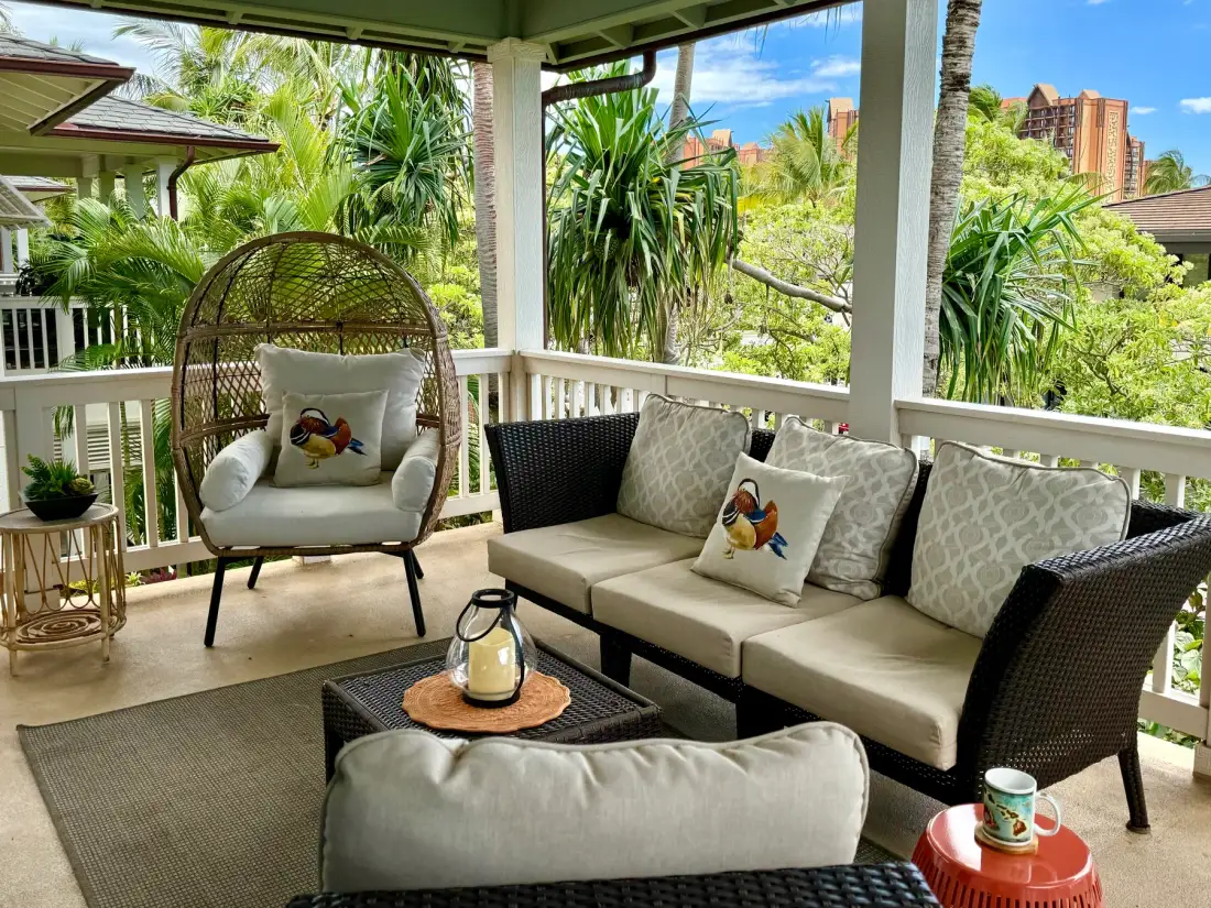 Una zona exterior cubierta con asientos de mimbre acolchados y vegetación tropical alrededor.