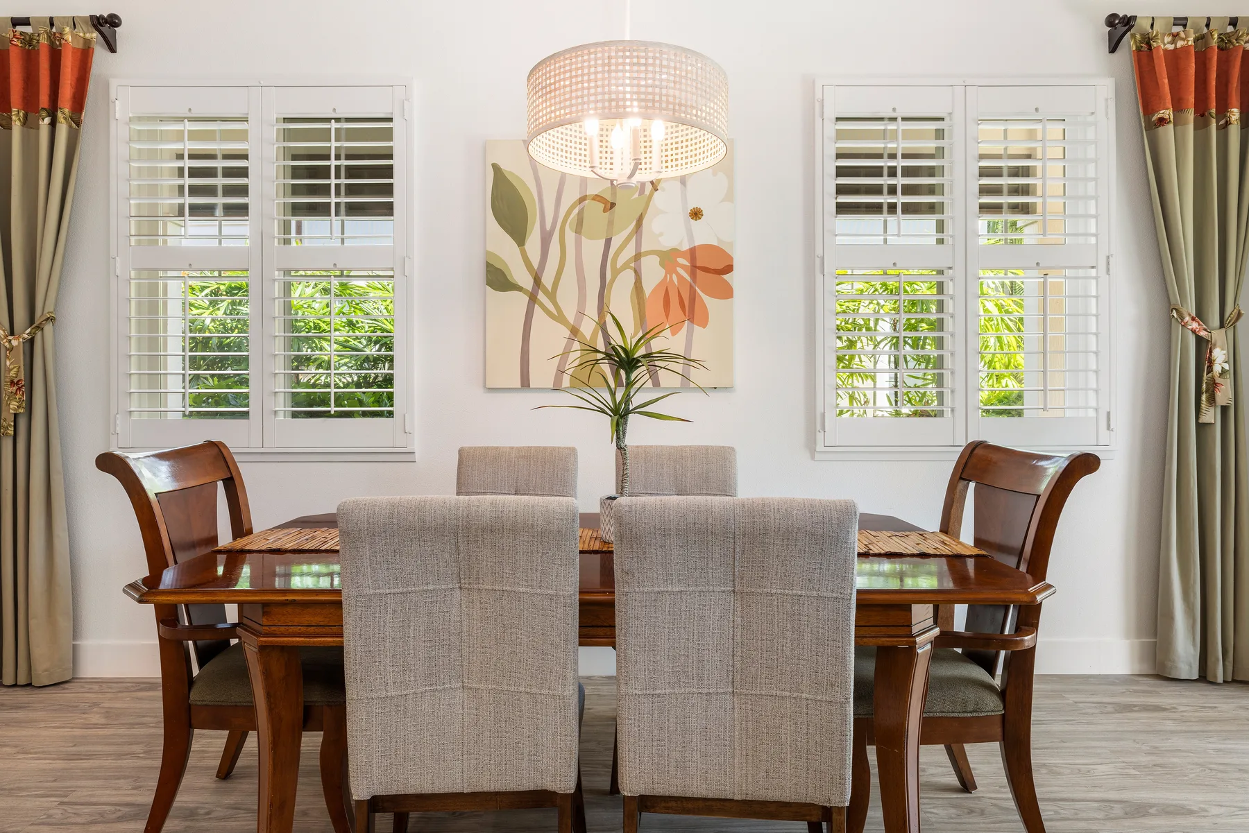 Un comedor con una mesa de madera, asientos tapizados y ventanas con persianas.