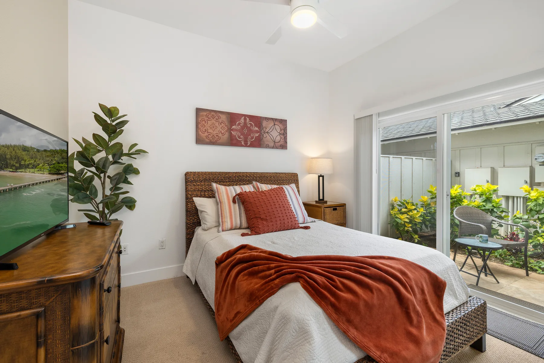 Un dormitorio con una cama, cojines estampados y puertas corredizas de vidrio que dan a un patio.