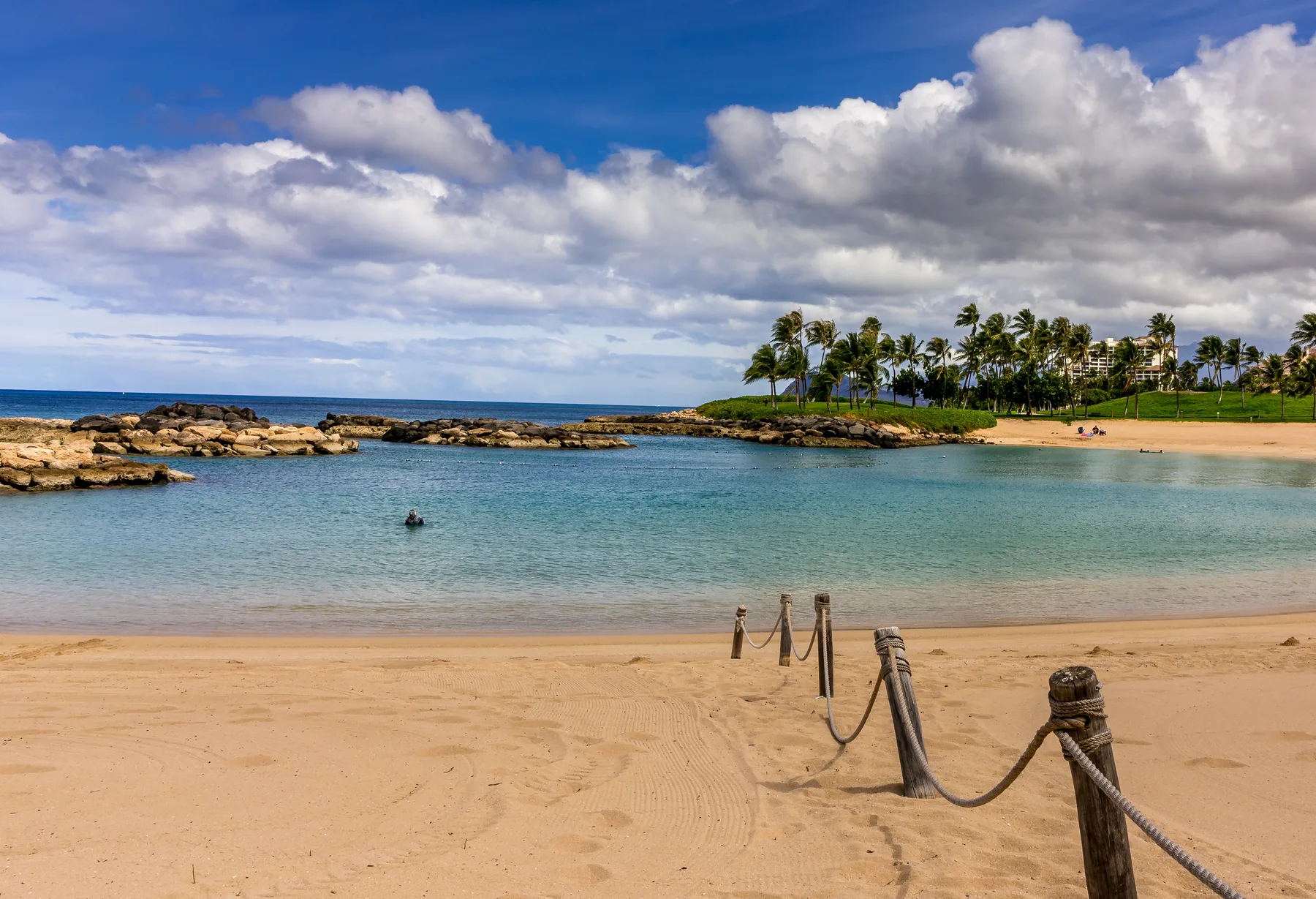 Una playa de arena bordea una laguna tranquila, con palmeras en la orilla distante.