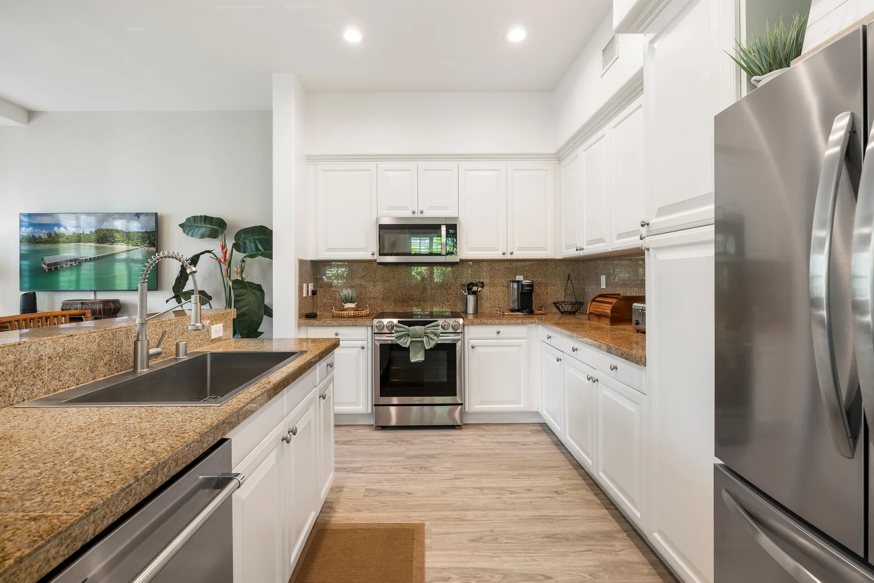 Una cocina luminosa con gabinetes blancos, encimeras de granito y electrodomésticos de acero inoxidable.