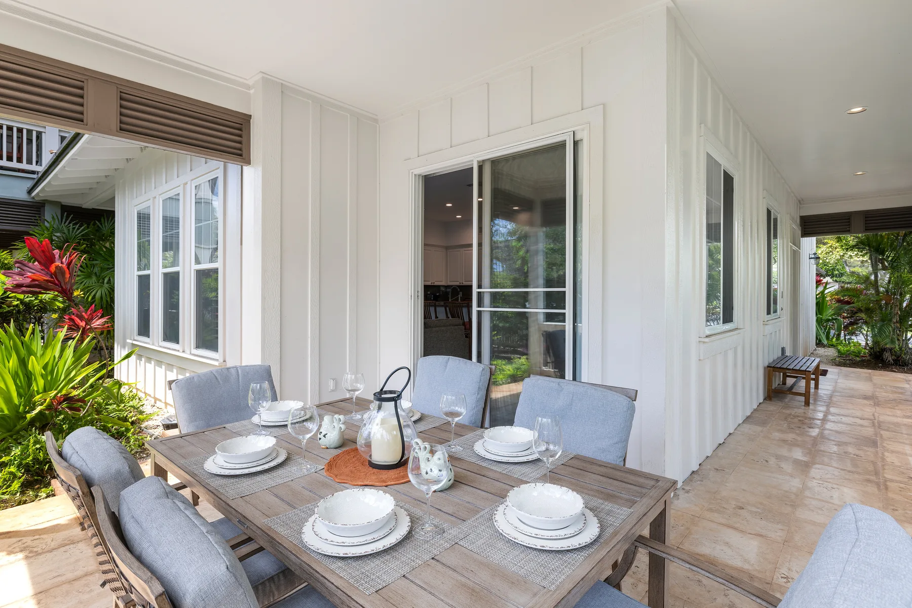 Comedor al aire libre junto a una casa blanca, con la mesa puesta y plantas de jardín.