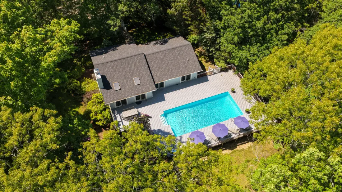 Una vista aérea muestra una casa junto a una piscina rodeada de árboles.