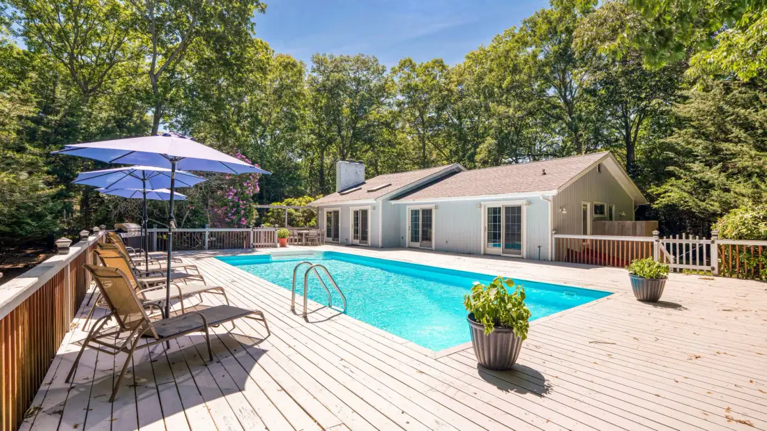 Una piscina exterior está junto a una amplia terraza y una casa baja.