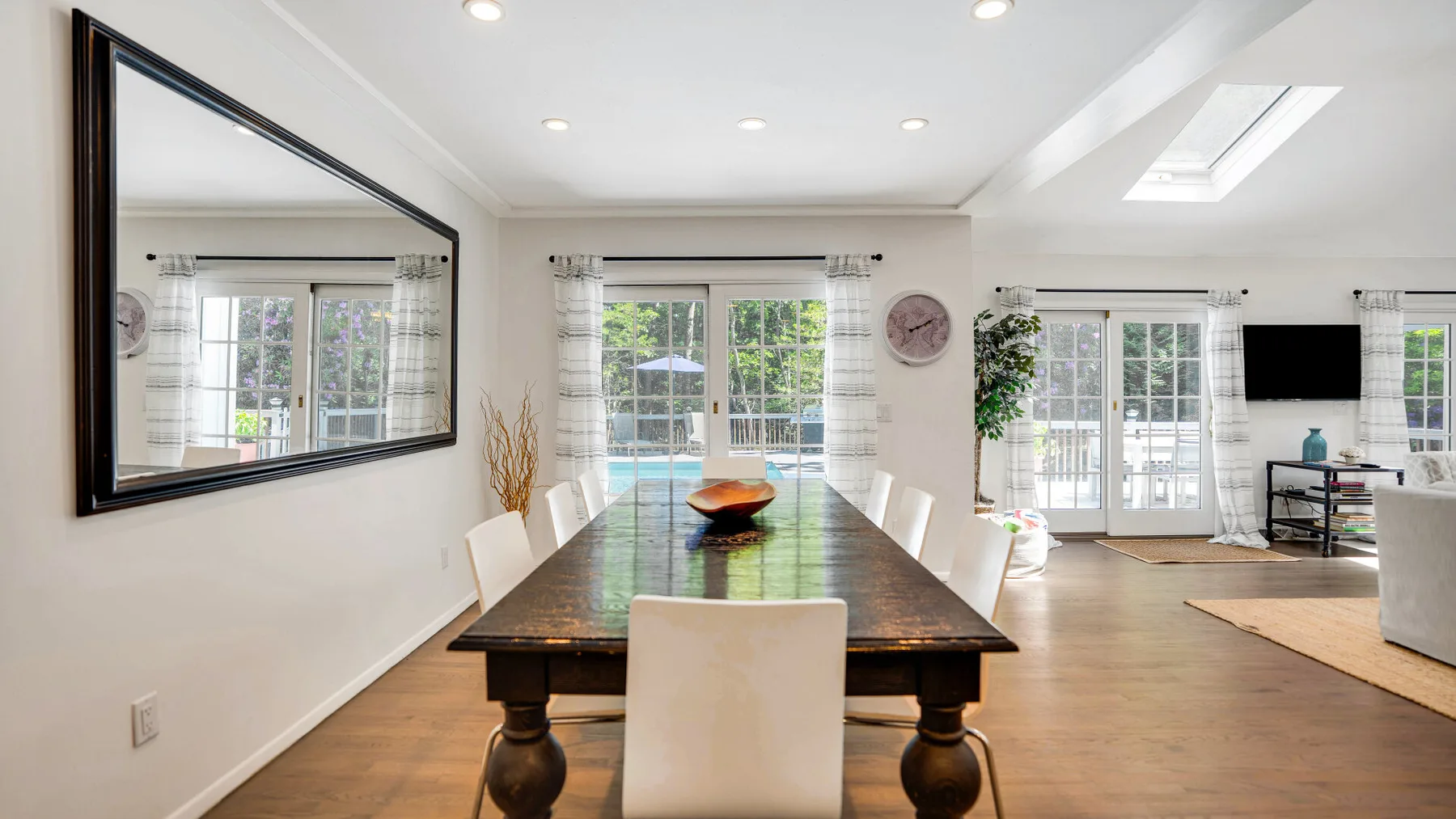 Comedor con una mesa larga, asientos blancos y ventanas grandes.