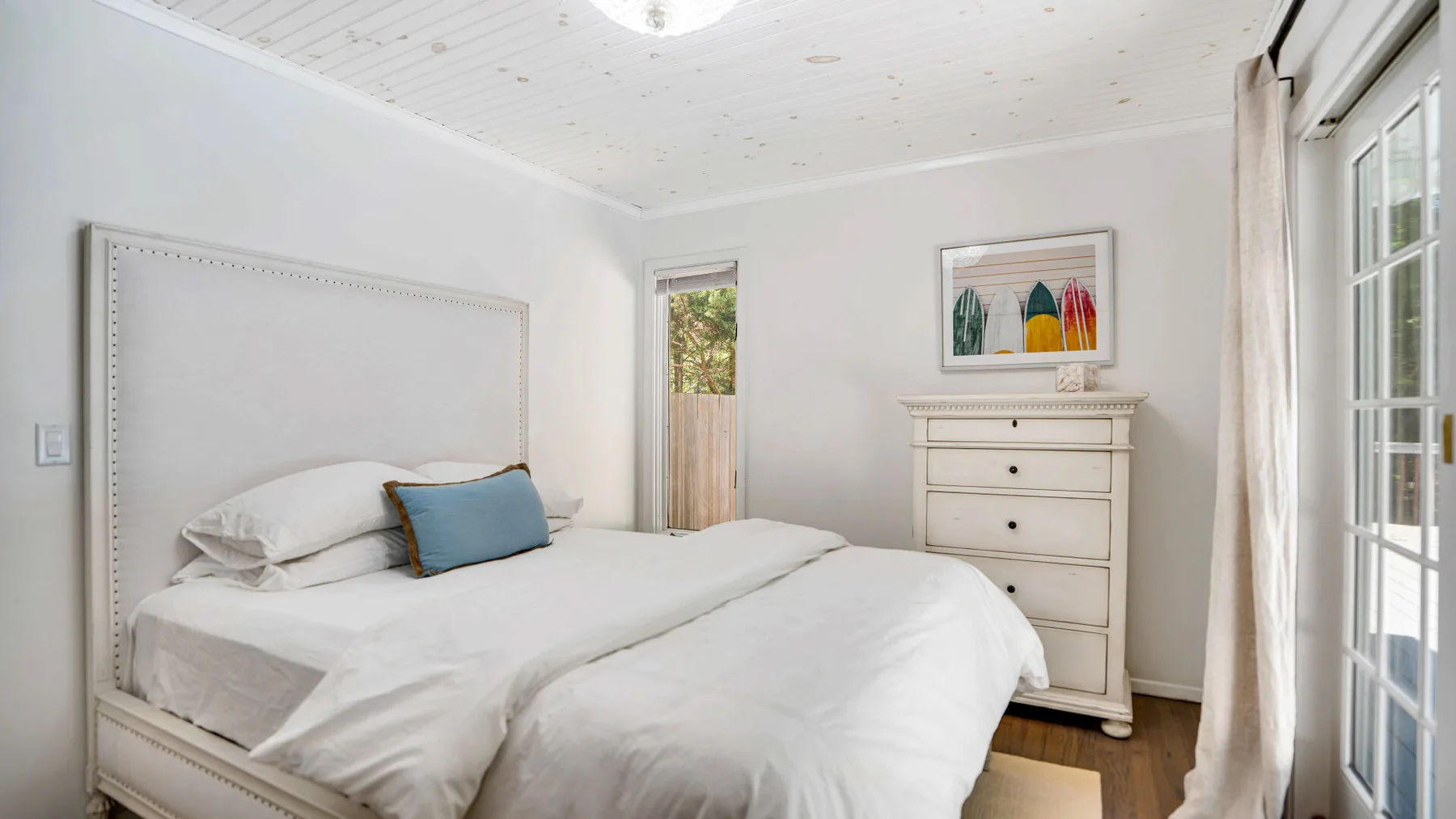 Un dormitorio luminoso con una cama arreglada y una cómoda.