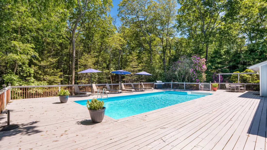 Una piscina está sobre una amplia terraza de madera rodeada de árboles.