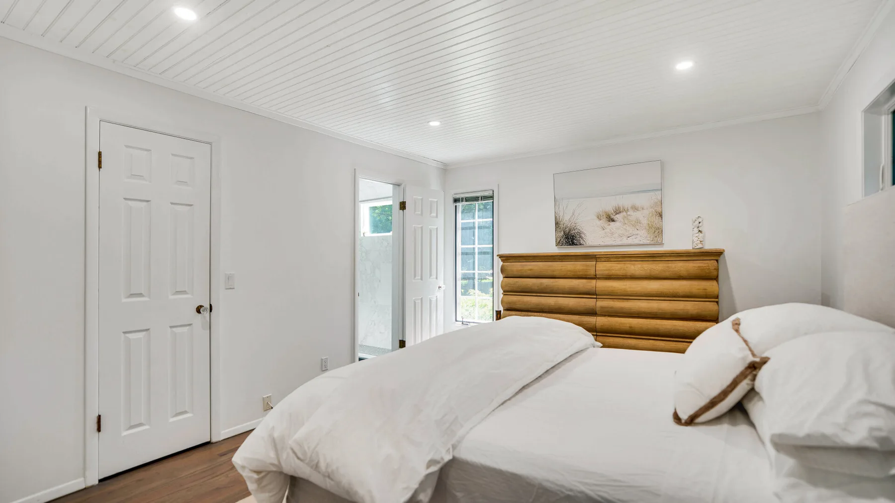 Un dormitorio luminoso con ropa de cama blanca y un cabecero de madera.