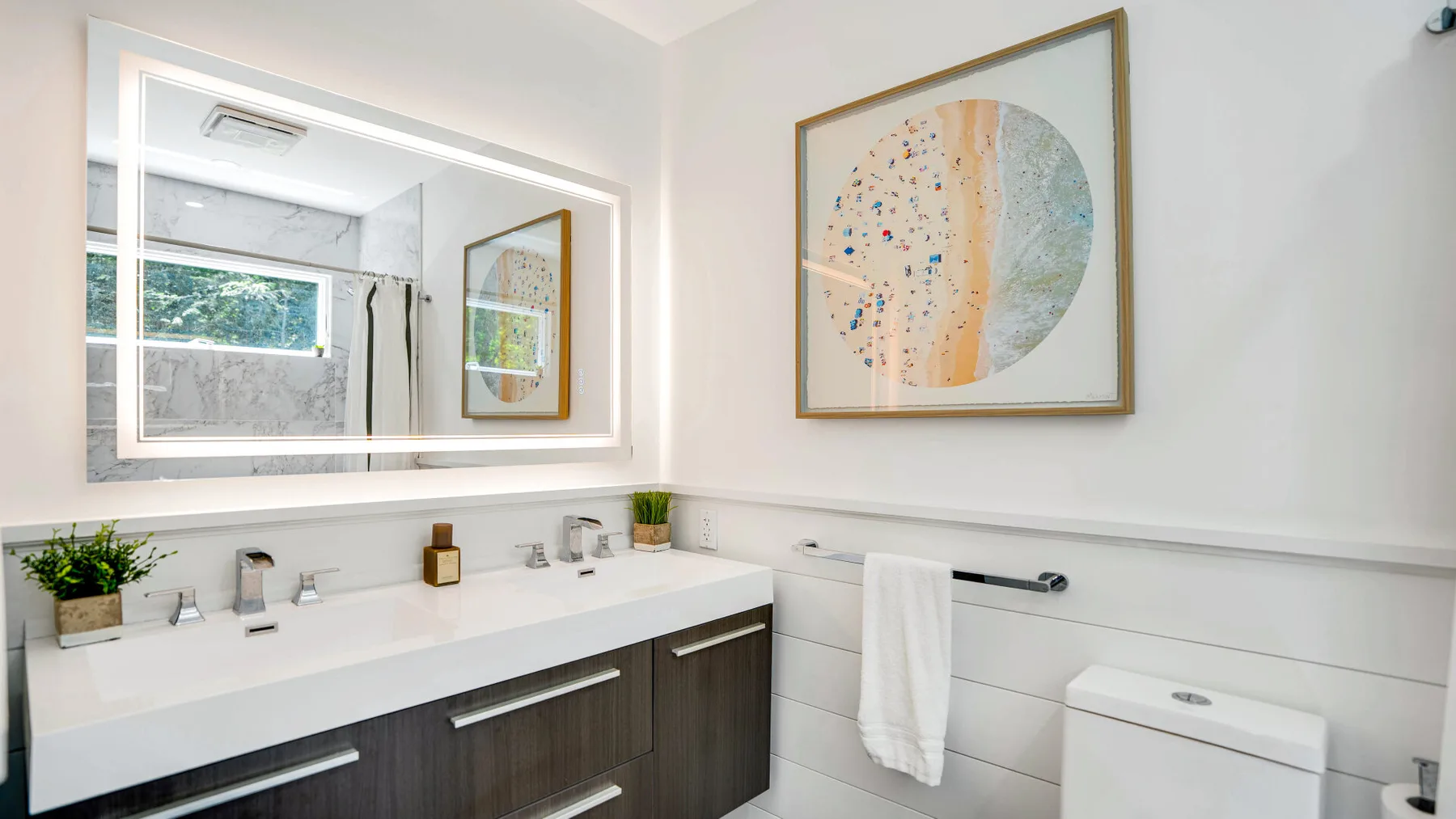 Un baño luminoso con una larga encimera de lavabo y un espejo grande.