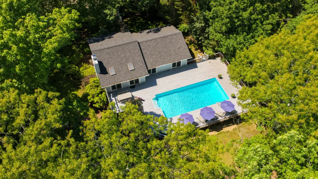 Una vista aérea muestra una casa junto a una piscina, rodeada de árboles.