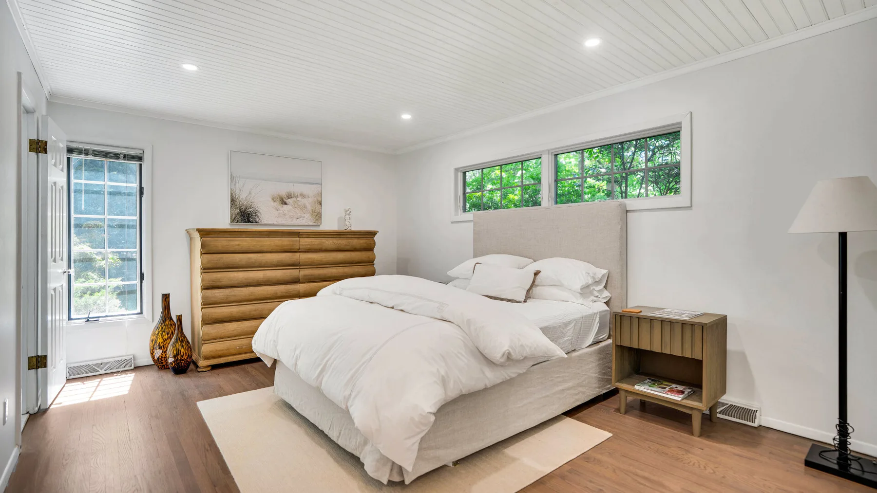 Un dormitorio luminoso con una cama, un cabecero de madera y ventanas.