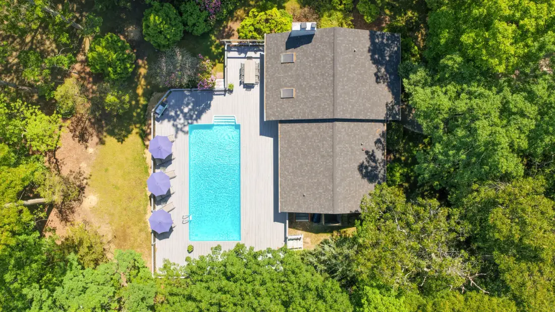 Una vista aérea muestra una casa junto a una piscina, rodeada de árboles.