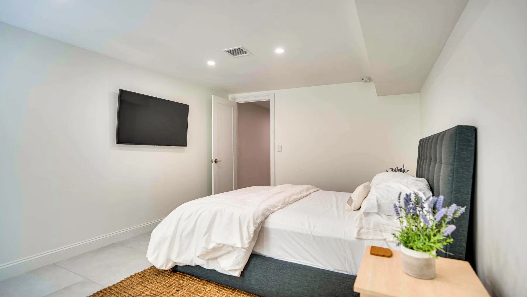 Un dormitorio luminoso con una cama, un televisor en la pared y una mesita de noche.