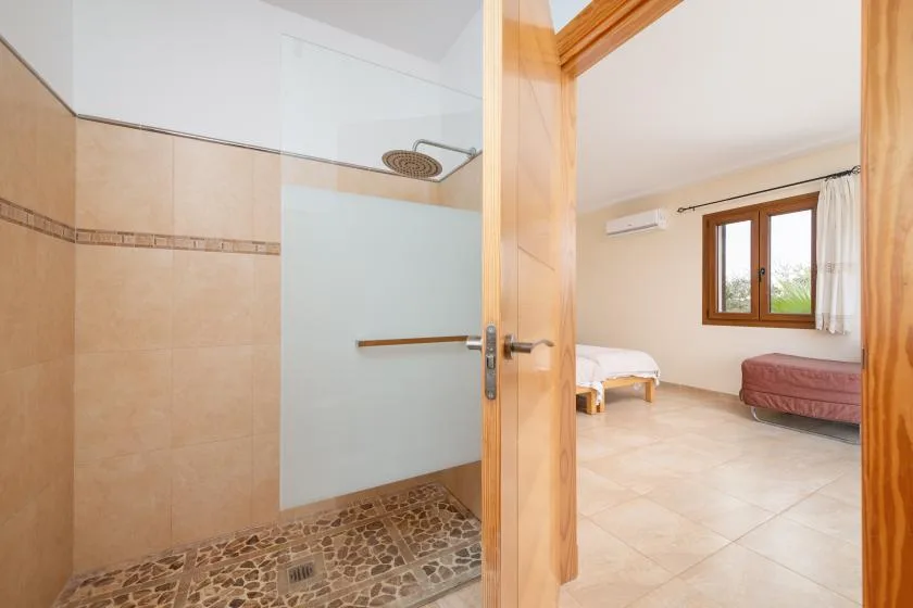 Se ve un dormitorio a través de una puerta abierta junto a una ducha con mampara de vidrio.