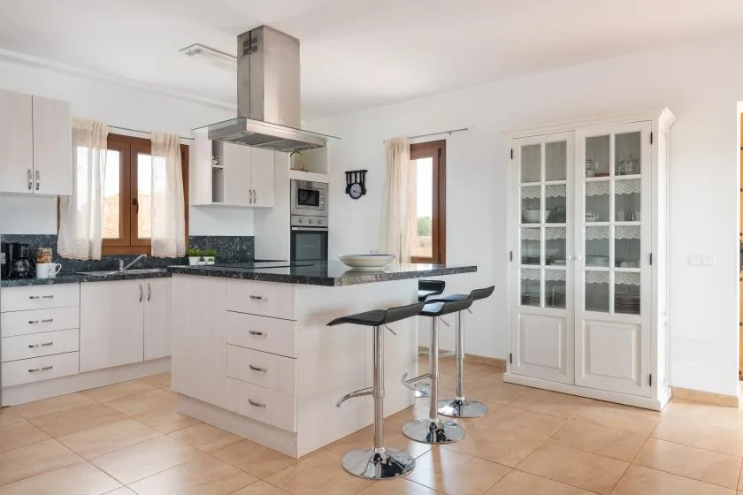 Una cocina luminosa con una isla central y dos taburetes de bar.