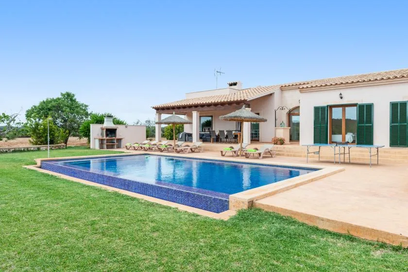 Una casa y una piscina están junto a un césped bajo un cielo despejado.