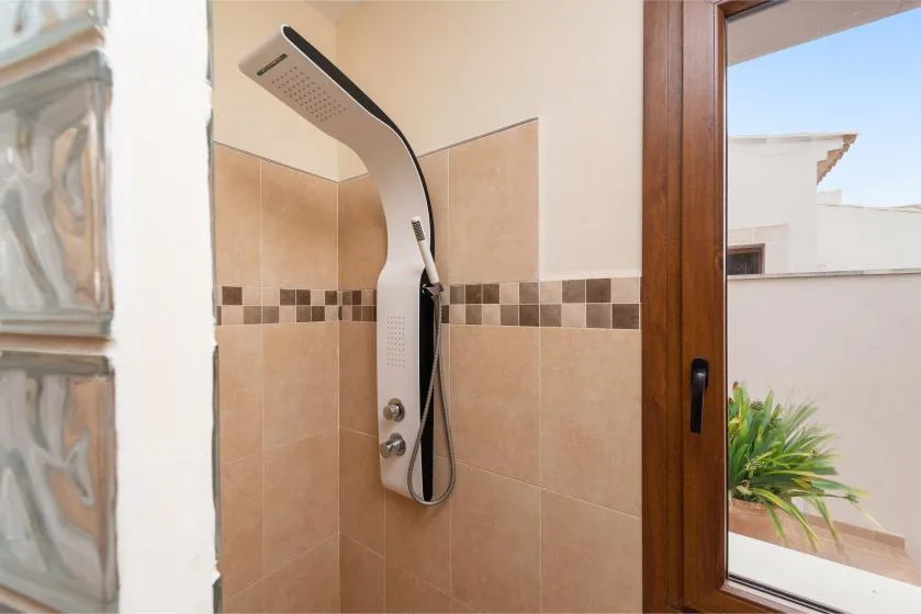 Una ducha con azulejos junto a una ventana con marco de madera y vegetación afuera.